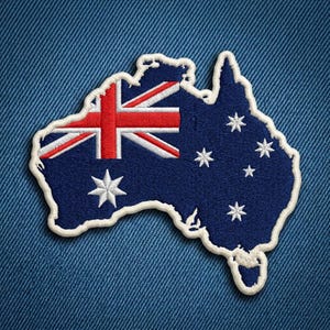 May include: An embroidered patch shaped like the continent of Australia, featuring the dark blue, red, and white Australian flag design. The patch has a thick, white stitched border and displays the Union Jack and white stars on a blue field.