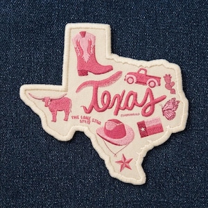May include: An embroidered patch shaped like the state of Texas on a cream background. It features pink icons including a cowboy boot, a longhorn, a pickup truck, a hat, a butterfly, a cactus, a star, and the Texas flag. The text reads Texas and The Lone Star State.