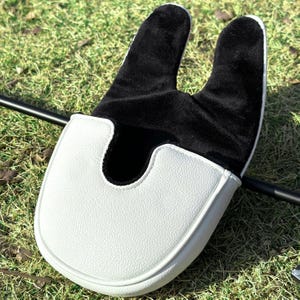May include: A mallet-style golf putter headcover featuring a white textured exterior and a soft black interior lining. The cover has a U-shaped opening designed to fit over the putter head, with a smooth, rounded front edge and a two-pronged top.