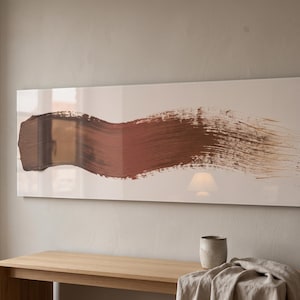 May include: A rectangular wall art piece featuring a single, wide, horizontal brushstroke in shades of brown and copper across a smooth, off-white background. The artwork has a glossy, reflective finish that captures light and surrounding room details.