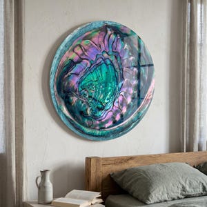 May include: A large circular wall art piece featuring a polished abalone shell surface with iridescent swirls of deep emerald green, vibrant violet, and soft pink tones. The shell displays a natural, organic texture with a glossy, reflective finish.
