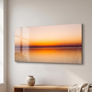 Puede incluir: Una impresión de arte mural rectangular que presenta un degradado horizontal de colores cálidos de atardecer, pasando de un tono melocotón pálido en la parte superior a una línea de horizonte naranja oscuro y violeta, reflejada en agua calma.