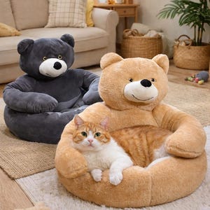 Pu&ograve; includere: Due letti per animali domestici a forma di orsacchiotto, uno grigio e uno beige, sono su un tappeto. Un gatto con pelo arancione e bianco riposa nel letto beige. I letti hanno una base rotonda e schienali a forma di testa di orso.