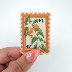 May include: Embroidered patch in the shape of a postage stamp. The patch features a design of orange blossoms with green leaves and the text "FL". The stamp reads "45¢" and has an orange border.