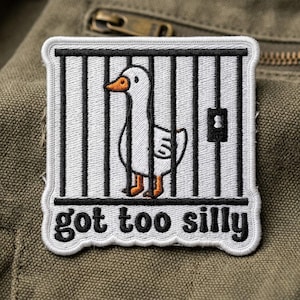 May include: Embroidered patch featuring a white goose inside a black and white cage. The goose has an orange beak and feet. The phrase "got too silly" is written in black, below the cage. The patch is bordered in white.