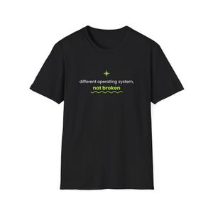Könnte beinhalten: Ein schwarzes kurzärmeliges T-Shirt mit einem Grafikdesign auf der Brust. Das Design zeigt ein kleines gelbes Sternsymbol über dem weißen Text "different operating system," gefolgt von dem grünen Text "not broken" über einer gelben Wellenlinie.