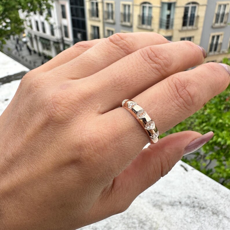 Puede incluir: Anillo de oro rosa con detalles de diamantes geom&eacute;tricos y en forma de coraz&oacute;n. El anillo se muestra en una mano, mostrando su dise&ntilde;o. Una pieza de joyer&iacute;a elegante.