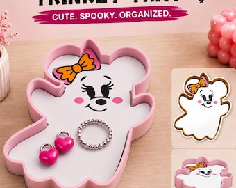 May include: A pink trinket tray shaped like a ghost with mouse ears and an orange bow. The tray features a white base with a printed ghost face, two pink heart-shaped charms, and a silver beaded ring. Text reads MOUSE GHOST TRINKET TRAY.