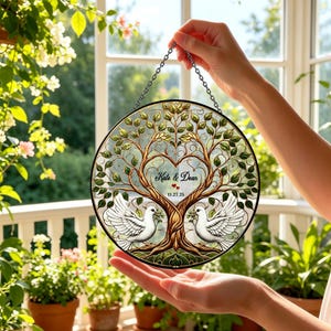 May include: A round stained glass panel featuring a tree with a heart-shaped design and the names "Kate & Dean" with a date. Two white doves are at the base of the tree. The panel is held by a chain.