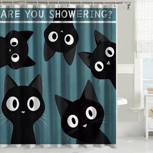Op de afbeelding: Een blauwgroen douchegordijn met vijf zwarte katten met grote witte ogen en de tekst ARE YOU SHOWERING? in het wit bovenaan gedrukt. De katten zijn in verschillende richtingen geplaatst, waaronder één die ondersteboven aan de bovenrand hangt.