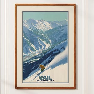 May include: A framed vintage travel poster for Vail, Colorado, USA. The artwork depicts a skier descending a snowy mountain slope, with a backdrop of snow-covered peaks under a blue sky. The poster has a brown wooden frame.