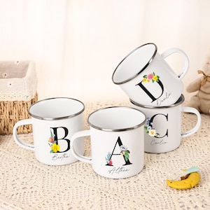 Può includere: Quattro tazze smaltate bianche con bordi argentati, ognuna con un'iniziale e un design floreale diverso. Le tazze hanno nomi stampati sotto le lettere. Le lettere sono nere e i fiori sono di vari colori. Le tazze sono impilate.