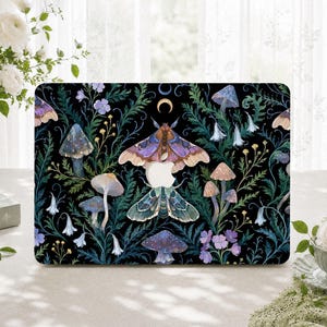 May include: A black laptop skin featuring a botanical pattern of purple and teal moths, various mushrooms, and small blue and yellow flowers. A crescent moon is positioned above the central moth, with a cutout for the apple logo in the middle.