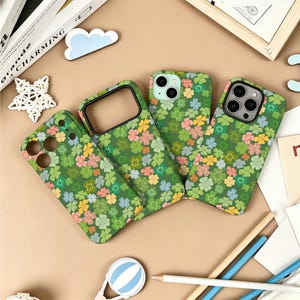 May include: Four mobile phone cases featuring a repeating pattern of four-leaf clovers in shades of green, pink, yellow, and light blue. The cases have cutouts for camera lenses and buttons, with varying layouts to accommodate different phone models.
