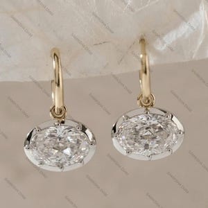 Op de afbeelding: Een paar gouden oorringen met ovale, heldere edelstenen. De edelstenen zijn gezet in een witmetalen montuur. De oorbellen zijn een soort sieraad.