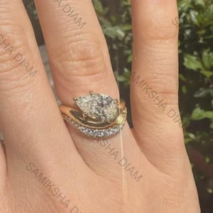 May include: A gold ring featuring a pear-shaped center stone set in a bypass style band. The band consists of two distinct sections: one smooth gold shank and one pavé-set band adorned with small, clear, sparkling stones along the outer edge.