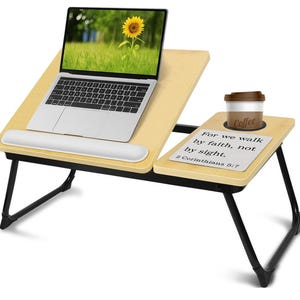May include: A light wood laptop desk with a black frame. A laptop with a sunflower image on the screen sits on the desk, along with a white wrist rest. A coffee cup and a notepad with text are on the side.