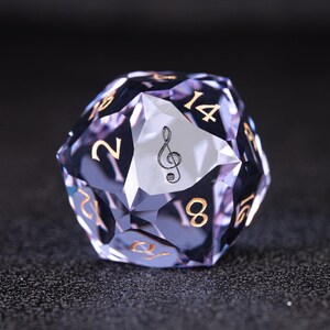 Puede incluir: Un dado D20 multifacético y transparente con tonos púrpuras y números dorados. Una cara presenta un símbolo de clave de sol negro. Diseñado para juegos de mesa, tiene una superficie facetada.