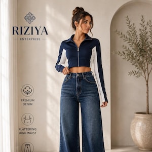 Op de afbeelding: Een marineblauw en wit kort jack met lange mouwen en rits, gecombineerd met een donkerblauwe high-waist spijkerbroek met wijde pijpen. De afbeelding bevat de tekst RIZIYA ENTERPRISE, PREMIUM DENIM, FLATTERING HIGH WAIST, WIDE LEG COMFORT en Effortless STYLE.