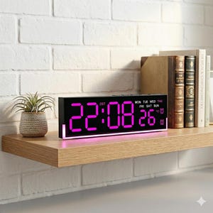 Könnte beinhalten: Ein schwarzer digitaler Wecker mit leuchtend rosa Ziffern, die die Uhrzeit und das Datum anzeigen. Die Uhr steht auf einem Holzregal mit einer kleinen Topfpflanze und Büchern. Die Uhrzeit ist 22:08 und das Datum ist der 26.