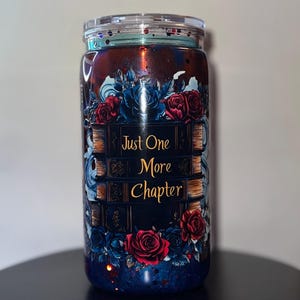 May include: A tumbler with a clear lid, featuring a dark blue and red design with floral accents. The tumbler is adorned with the text "Just One More Chapter" in gold lettering, surrounded by illustrations of books and roses.