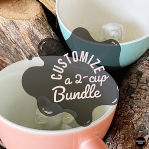May include: Two ceramic mugs with a white interior and a 3D animal design. The mugs are pink and blue. The text "Customize a 2-cup Bundle" is superimposed on the image.