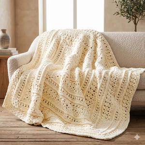 Puede incluir: Manta de ganchillo color crema sobre un sofá beige. La manta presenta un diseño de tejido abierto y texturizado con un patrón repetitivo. Los tonos suaves y neutros de la manta crean una estética acogedora y acogedora. La manta está hecha de hilo grueso.