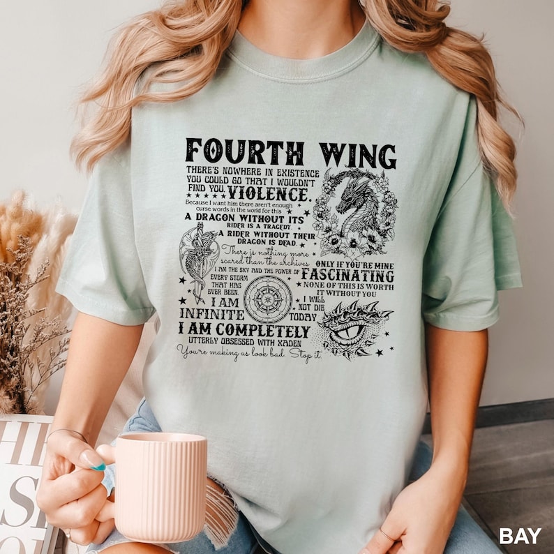May include: A light green t-shirt with the text "FOURTH WING" and other text and graphics. The design includes a dragon, stars, and the phrases "I AM INFINITE" and "I AM COMPLETELY UTTERLY OBSESSED WITH XADEN".