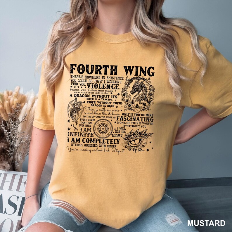 May include: Mustard-colored t-shirt featuring the text "Fourth Wing" and various graphic elements, including a dragon, compass, and eye. The shirt has multiple lines of text with phrases like "Violence" and "I am Infinite."