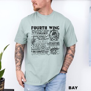 May include: A light green t-shirt with the text "FOURTH WING" and other phrases in black. The shirt features a dragon graphic and other decorative elements. The shirt is worn by a person.