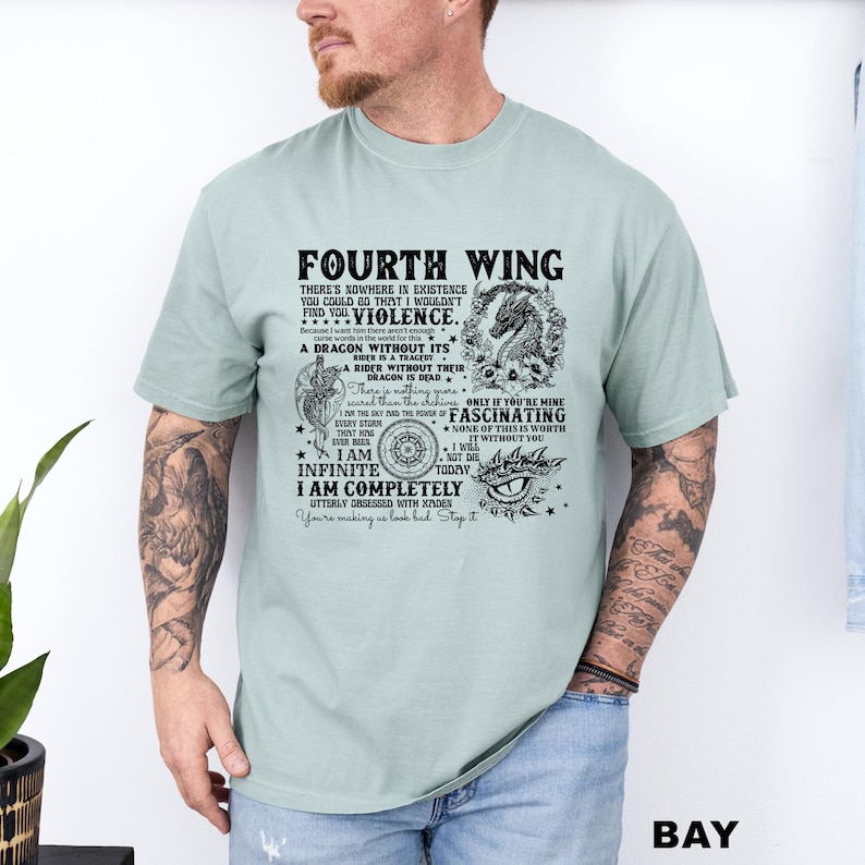 May include: A light green t-shirt with the text "FOURTH WING" and other phrases in black. The shirt features a dragon graphic and other decorative elements. The shirt is worn by a person.