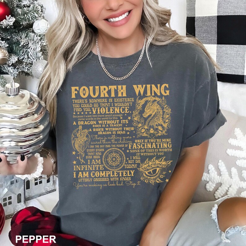 May include: Dark gray t-shirt with the text "FOURTH WING" in gold lettering. The shirt features a dragon graphic and additional text. The shirt is a comfortable, casual style.