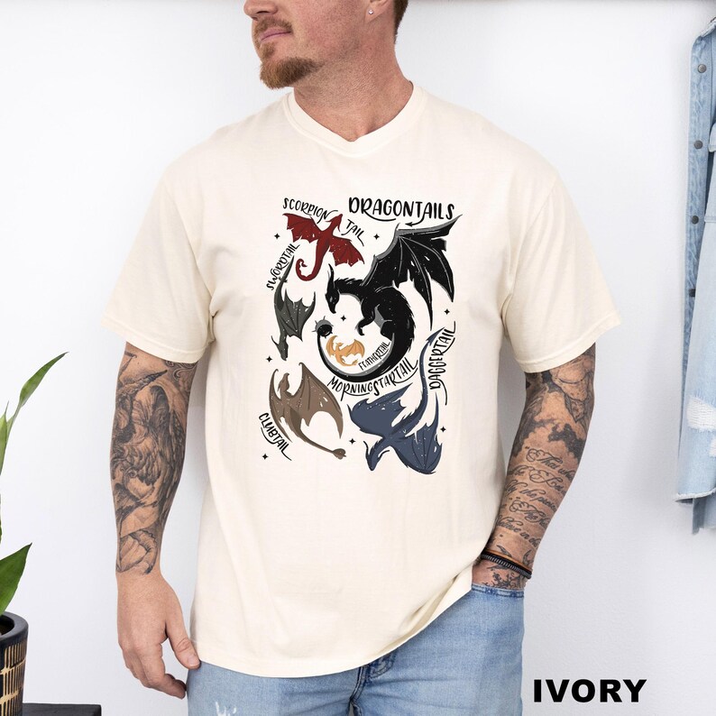 以下が含まれることがあります： アイボリー色のTシャツ。ドラゴン柄と「DRAGONTAILS」の文字がプリントされています。デザインには、「SCORPION TAIL」や「MORNINGSTARTAIL」などの名前が付いた様々なドラゴンのイラストが含まれています。柔らかい素材のシャツです。
