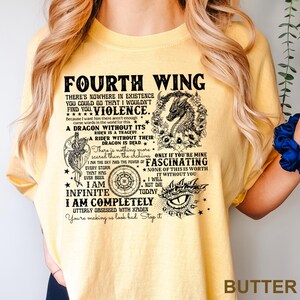 May include: Butter-colored t-shirt with black text and graphics. The text reads "FOURTH WING" and includes phrases like "A DRAGON WITHOUT ITS" and "I AM INFINITE." The design features a dragon, stars, and other decorative elements.