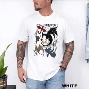 以下が含まれることがあります： 白のTシャツ。赤、黒、茶色、青のドラゴンイラストが描かれた「DRAGONTAILS」のデザイン。Tシャツの下部には「WHITE」の文字がプリントされています。
