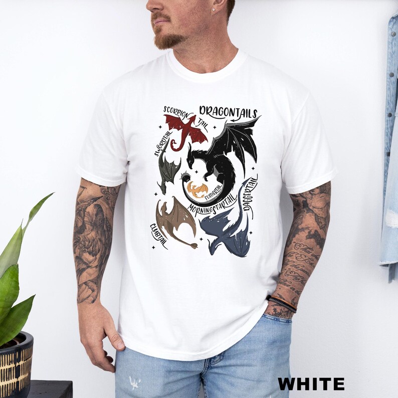 以下が含まれることがあります： 白のTシャツ。赤、黒、茶色、青のドラゴンイラストが描かれた「DRAGONTAILS」のデザイン。Tシャツの下部には「WHITE」の文字がプリントされています。
