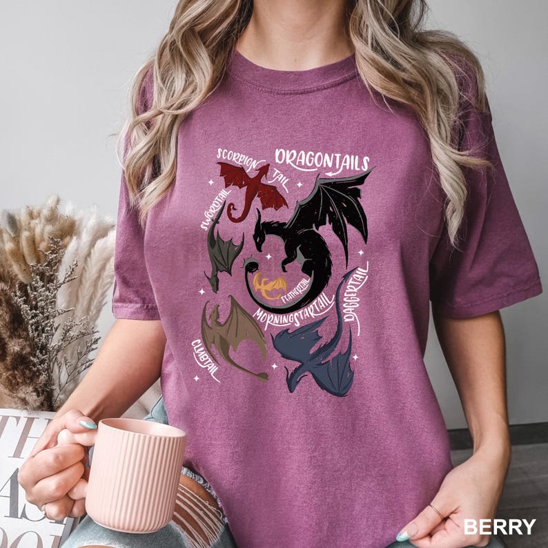 以下が含まれることがあります： ベリー色のTシャツ。デザインには「DRAGONTAILS」の文字と、さまざまなドラゴンのイラストが描かれています。各ドラゴンは異なる種類の尾でラベル付けされています。Tシャツはベリー色です。