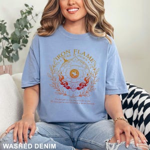 May include: Light blue washed denim t-shirt with a graphic design. The design features the text "IRON FLAME TURN IT DOWN" around a circular emblem with flames and a bird. Below the emblem is text. The shirt is a relaxed fit.