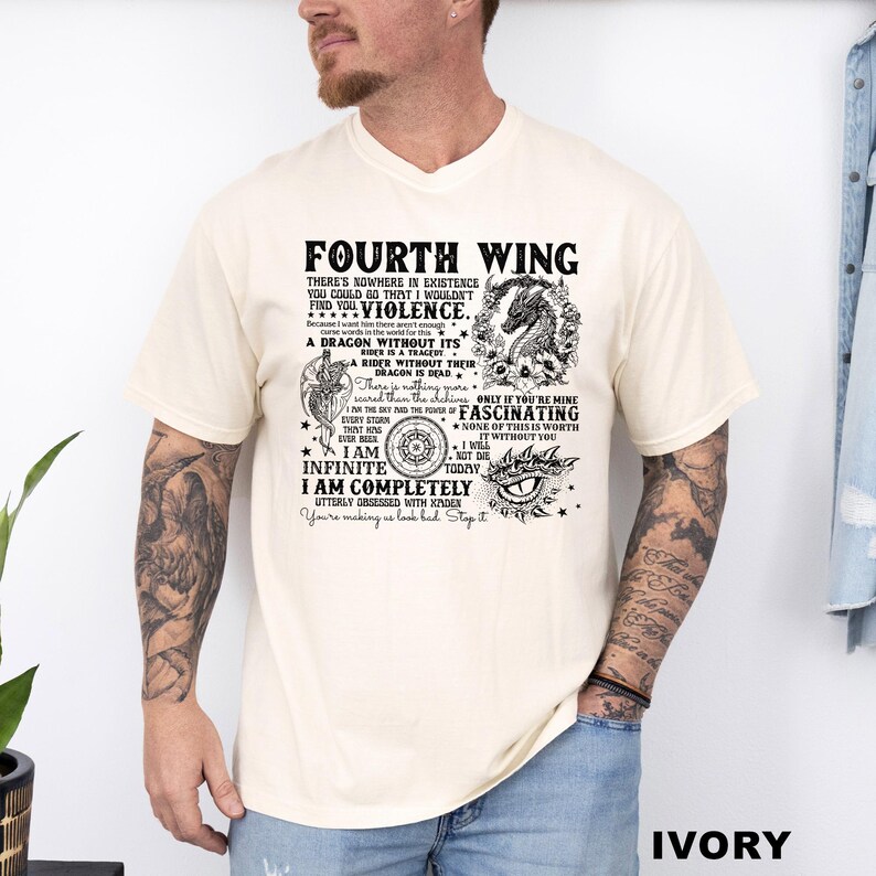May include: Ivory-colored t-shirt with the text "FOURTH WING" and various phrases and graphics. The design includes a dragon, compass, and eye. The shirt is a crew neck and has short sleeves.