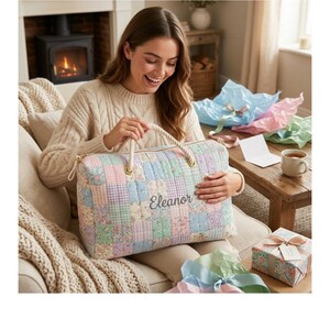 May include: A quilted patchwork duffel bag with the name "Eleanor" embroidered on the front. The bag features a variety of pastel-colored squares and rope handles. The bag is approximately 12 inches long.