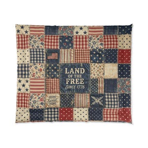 May include: A patchwork quilt with a patriotic theme. The quilt features squares of red, white, and blue fabrics with stars, stripes, and floral patterns. The center square reads "Land of the Free Since 1776."