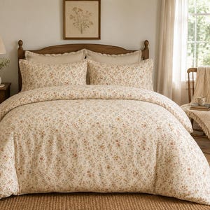Puede incluir: Un juego de cama que incluye una funda nórdica y dos fundas de almohada a juego con una base de color crema y un patrón floral denso y pequeño en tonos apagados de óxido, azul y verde. La tela de todo el conjunto tiene una textura mate suave.