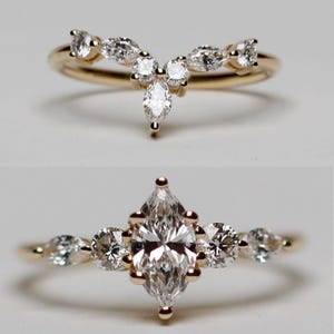 Könnte beinhalten: Zwei goldene Ringe mit klaren Edelsteinen. Der obere Ring ist ein gebogenes Band mit mehreren kleinen Steinen. Der untere Ring hat einen großen, marquiseförmigen Mittelstein, flankiert von kleineren runden Steinen, alle in Gold gefasst.