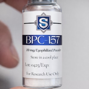 May include: A clear glass vial containing white lyophilized powder with a white label featuring a blue shield logo with the letter S. The text reads BPC-157, 10 mg/Lyophilized Powder, Store in a cool place, Lot: 0425/Exp:, and For Research Use Only.