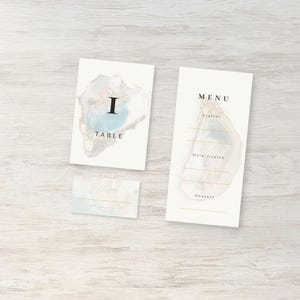 May include: Elegant wedding stationery set featuring a table number card, menu card, and place card. The cards have a watercolor design with blue, gold, and beige tones. The table card displays the number "I" and the word "TABLE". The menu card lists "MENU".