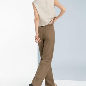 May include: A sleeveless, beige linen top paired with brown linen trousers. The trousers have a straight leg design. The outfit is simple and elegant, suitable for casual or semi-formal occasions.