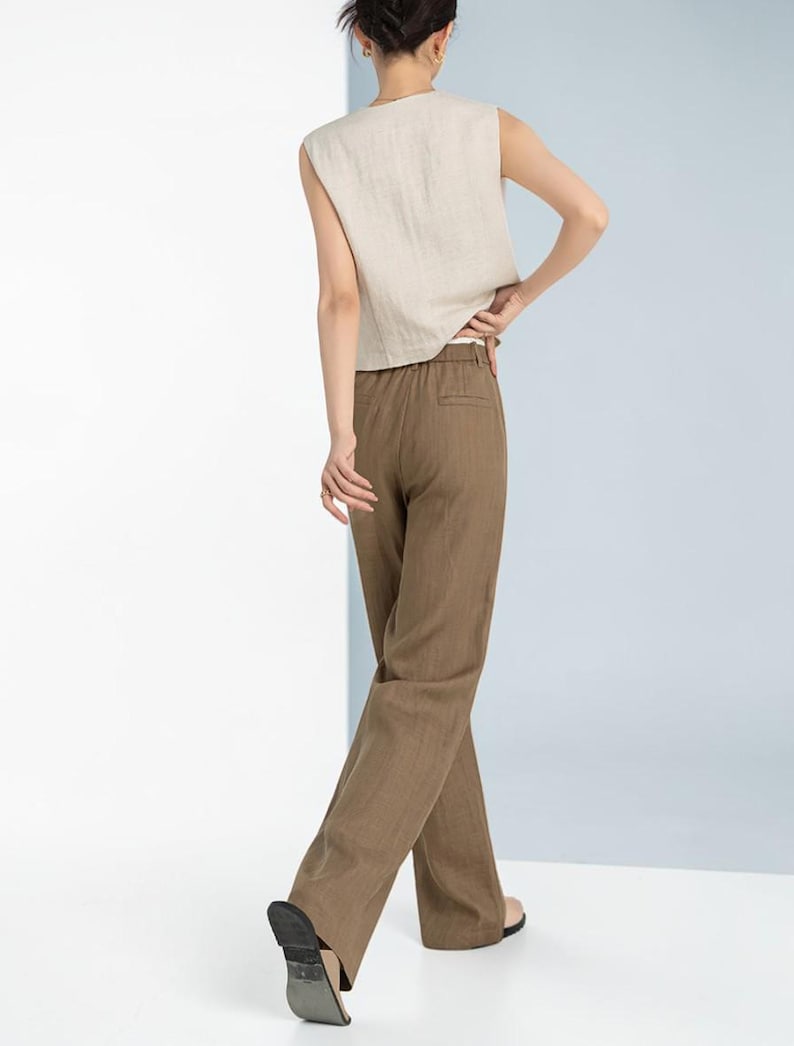 May include: A sleeveless, beige linen top paired with brown linen trousers. The trousers have a straight leg design. The outfit is simple and elegant, suitable for casual or semi-formal occasions.