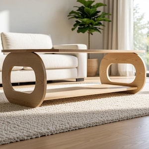 Puede incluir: Una mesa de centro de madera de color claro con una superficie rectangular lisa y un estante inferior, sostenida por dos paneles laterales redondeados de forma ovalada con centros abiertos, mostrando un acabado de veta natural.