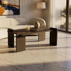 May include: A dark brown wooden coffee table with a rectangular top and wide, flat legs. The table is positioned in a room with light-colored marble flooring, featuring a clear glass candle holder and a small ceramic vase on its surface.