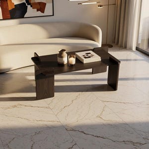 May include: A dark brown wooden coffee table with a rectangular top and two vertical side supports. On the table sits a small ceramic vase, a glass candle holder with a lit candle, and a white book. The table rests on a light marble floor.